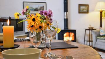 Un coin repas chaleureux, agrémenté d’une bougie, d’un vase de fleurs et d’une cheminée en arrière-plan.