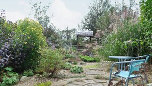 Un jardí amb un camí de pedra, un cobert i una cadira blava.