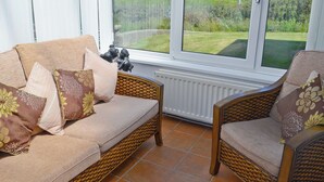 Ett ljust rum med en soffa och en fåtölj placerade framför ett stort fönster med utsikt över en gräsklädd äng.