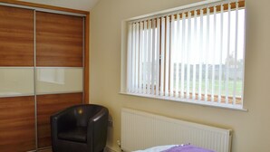 Ein Schlafzimmer mit Bett, Stuhl, Kleiderschrank und einem Fenster mit Jalousien.