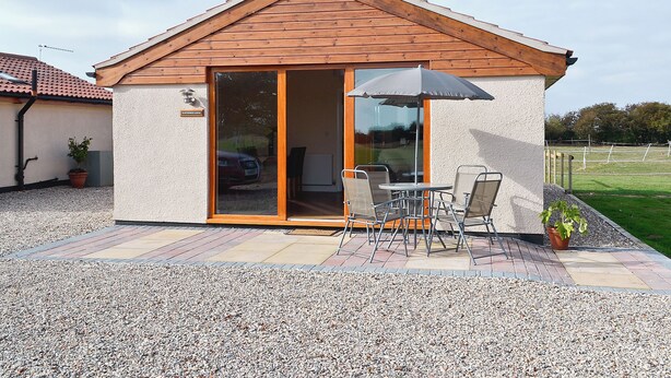 Ein kleines Haus mit Ziegeldach, einer Terrasse mit Tisch und Stühlen und einer Glastür zum Innenbereich.