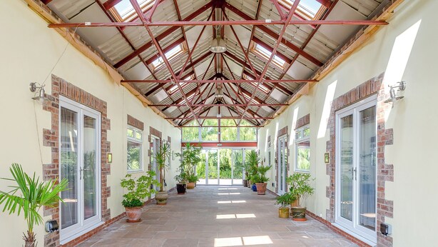 Un couloir couvert, doté d’un sol carrelé, de plantes en pot et de portes vitrées de part et d’autre.