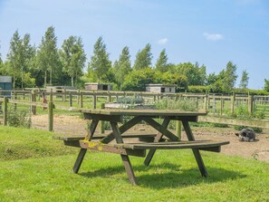 Una mesa de picnic en un área exterior cercada, con un campo de césped y árboles al fondo.