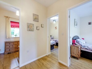 Un dormitorio con cama, mesita de noche y cómoda. Hay una ventana con cortina roja y un cuadro en la pared.