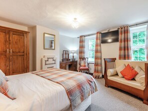 A bedroom with a bed, a wooden wardrobe, a desk with a chair, a sofa, and a window with curtains.