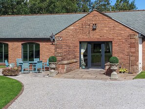 A brick building with a tiled roof, a patio with blue chairs, and potted plants.
