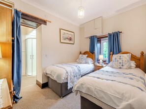 Un dormitorio con dos camas, un armario de madera, una mesita de noche con lámpara y una ventana con cortinas.