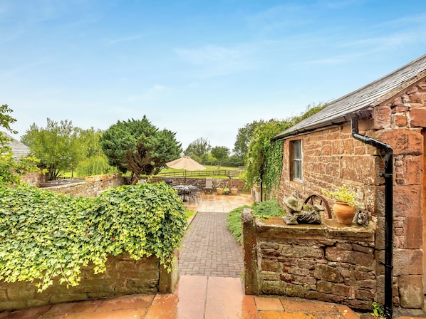 A stone building with a brick pathway leading to a patio area with outdoor furniture.
