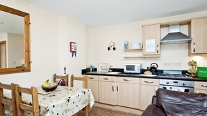 A compact kitchen with wooden cabinets, a microwave, and a stove. There is a dining table with chairs and a brown leather sofa.
