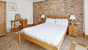 A bedroom with a wooden bed, two bedside tables with lamps, a wooden dresser, and a brick wall.