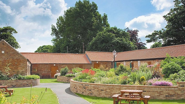 A courtyard with brick buildings, a paved walkway, and outdoor seating areas.