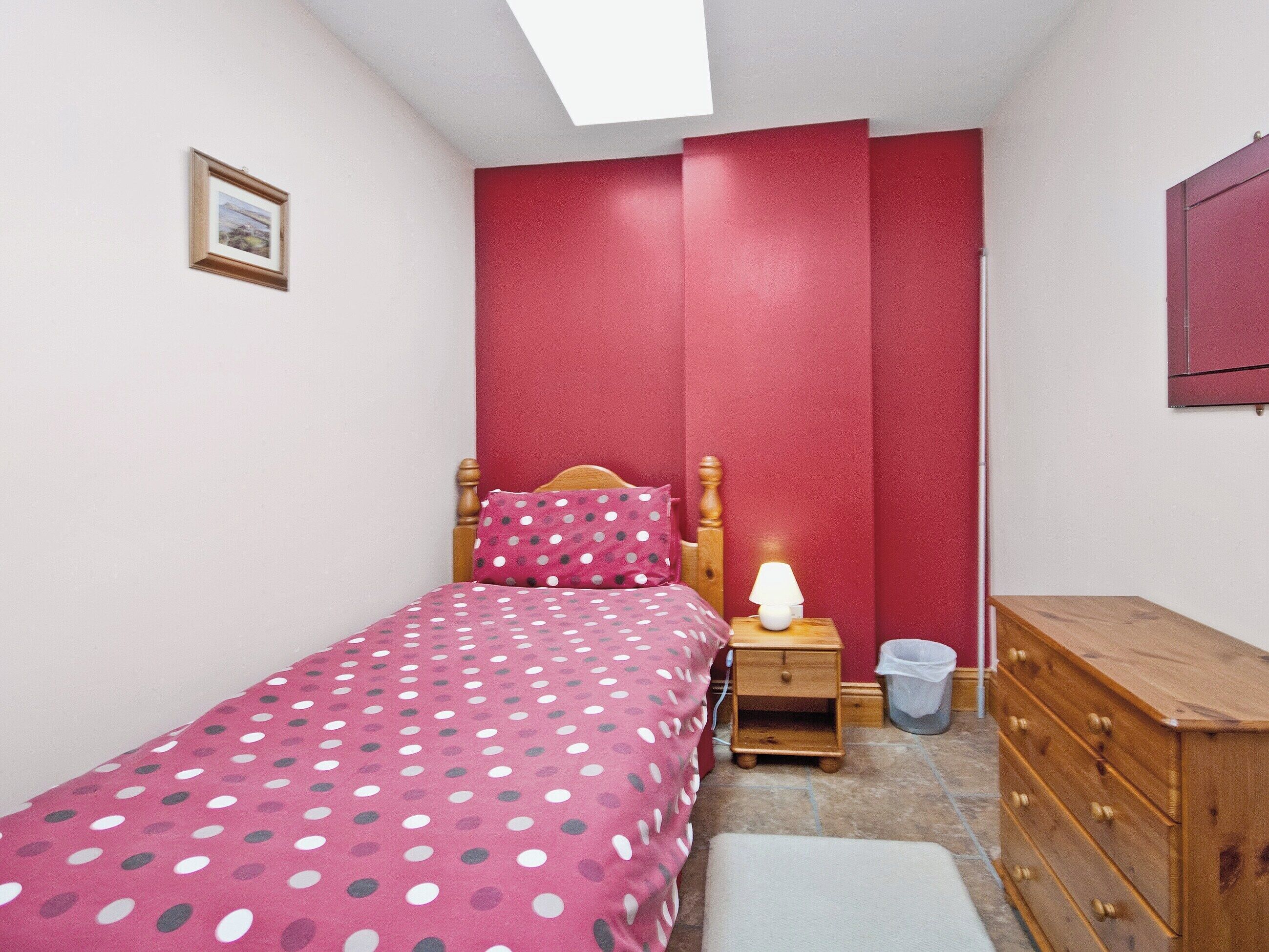 Ein kleines Schlafzimmer mit einem Bett, einem Nachttisch, einer Kommode, einem an der Wand montierten Fernseher und einem Bilderrahmen.