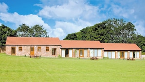 A two-story brick building with a red-tiled roof, multiple windows, and a grassy lawn in front.