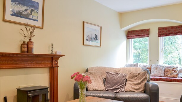 A cozy living room with a fireplace, a sofa, a wooden table, and a vase of flowers. - 3 bedroom accommodation in Ullswater, near Glenridding (Ullswater, near Glenridding)
