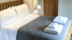 Un lit bien fait, avec du linge de lit blanc et une couverture grise, une lampe de chevet et une porte en bois avec une poignée noire.