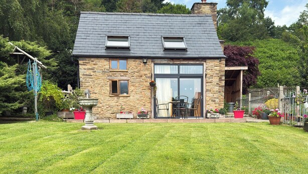 A stone house with a sloped roof, a large glass door, and a small patio with outdoor furniture. - 1 bedroom accommodation in Bircher Common, near Leominster (Bircher Common, near Leominster)