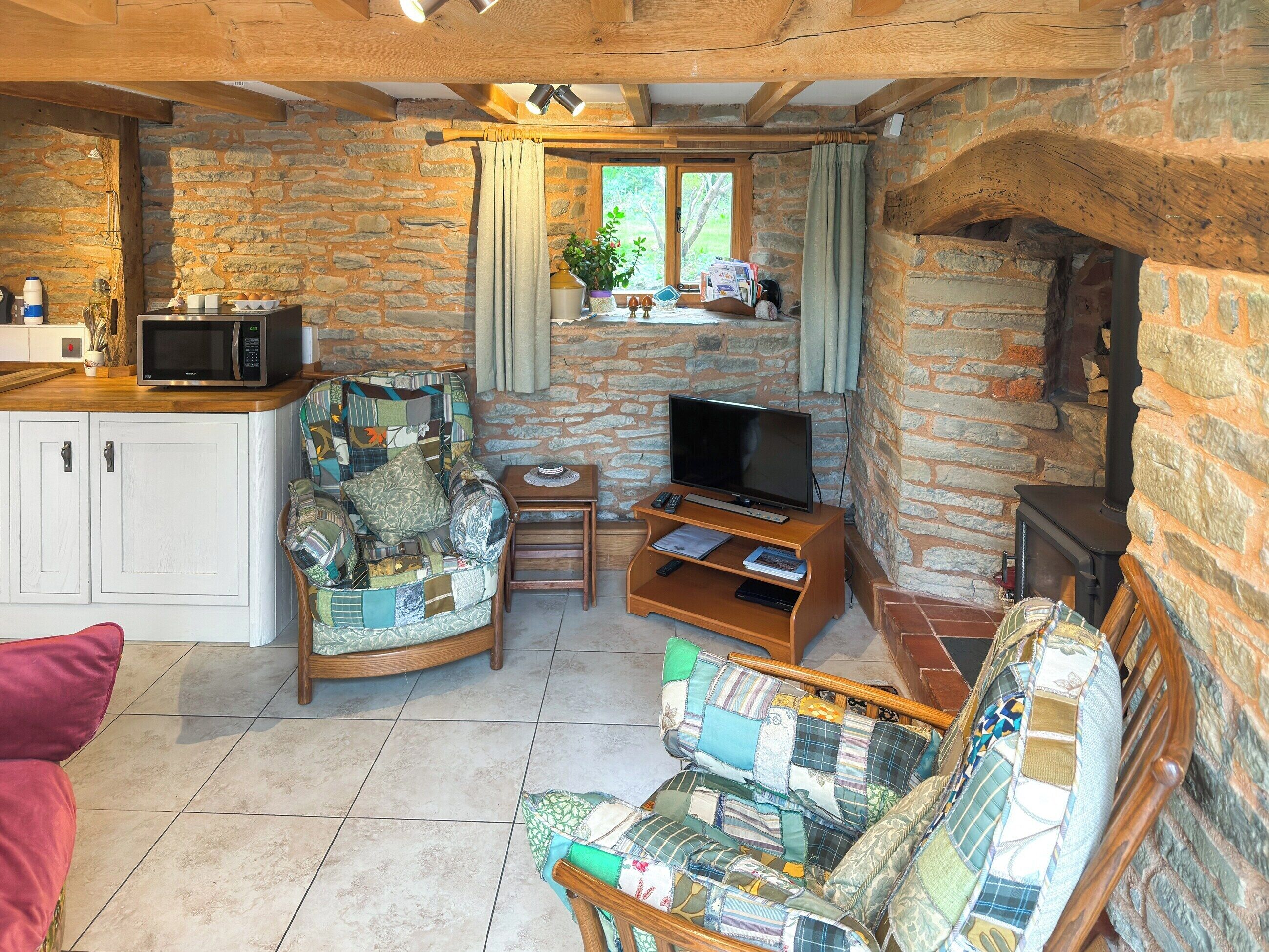 A cozy living room with a stone wall, a wooden ceiling, a television, a small table, and a sofa with a patchwork cover.