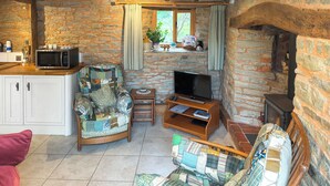 A cozy living room with a stone wall, a wooden ceiling, a television, a small table, and a sofa with a patchwork cover. - 1 bedroom accommodation in Bircher Common, near Leominster (Bircher Common, near Leominster)