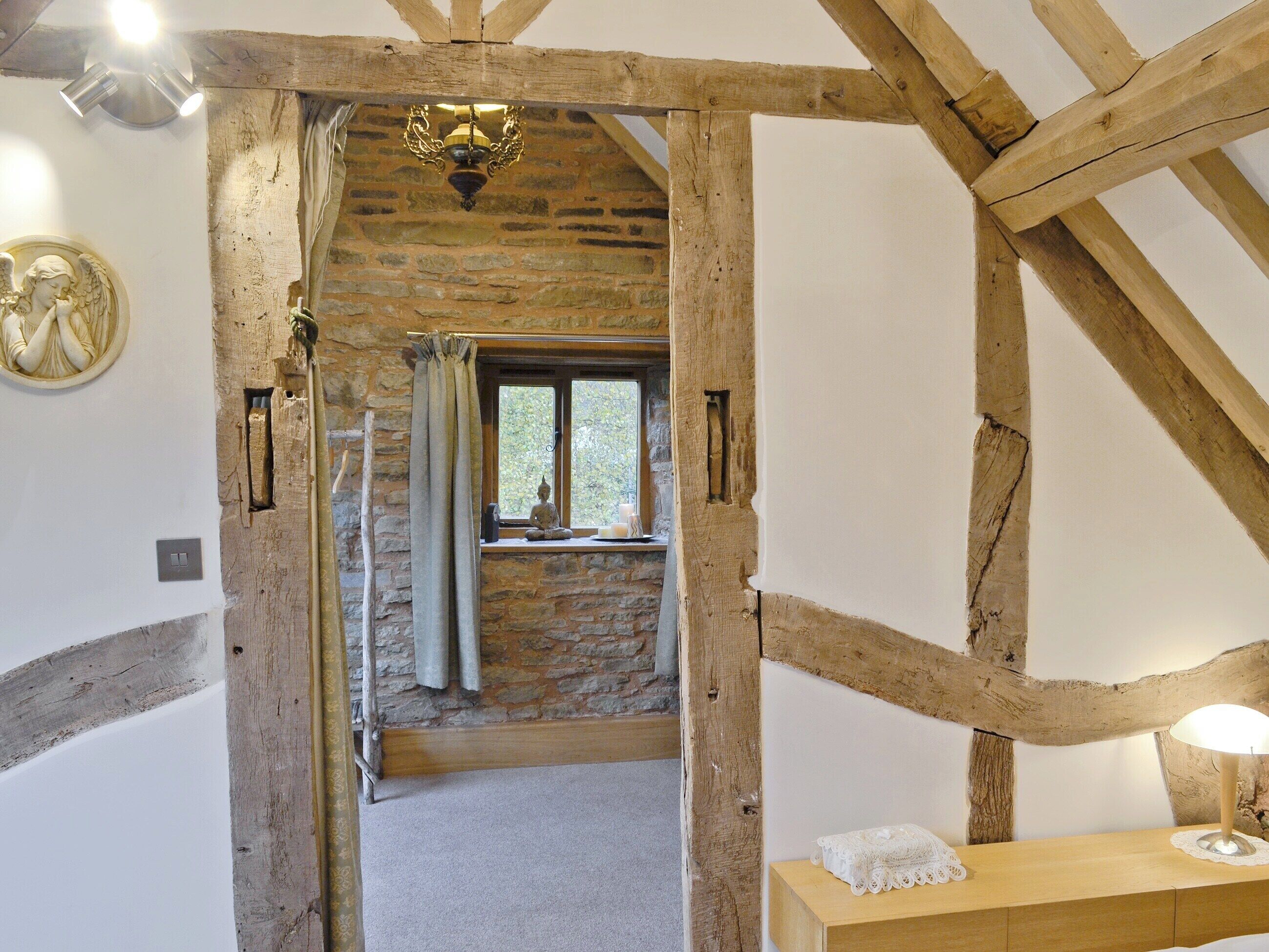 A rustic room with exposed wooden beams, a stone wall, and a window with a view of greenery.