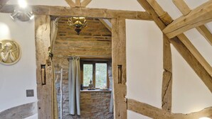 A rustic room with exposed wooden beams, a stone wall, and a window with a view of greenery. - 1 bedroom accommodation in Bircher Common, near Leominster (Bircher Common, near Leominster)