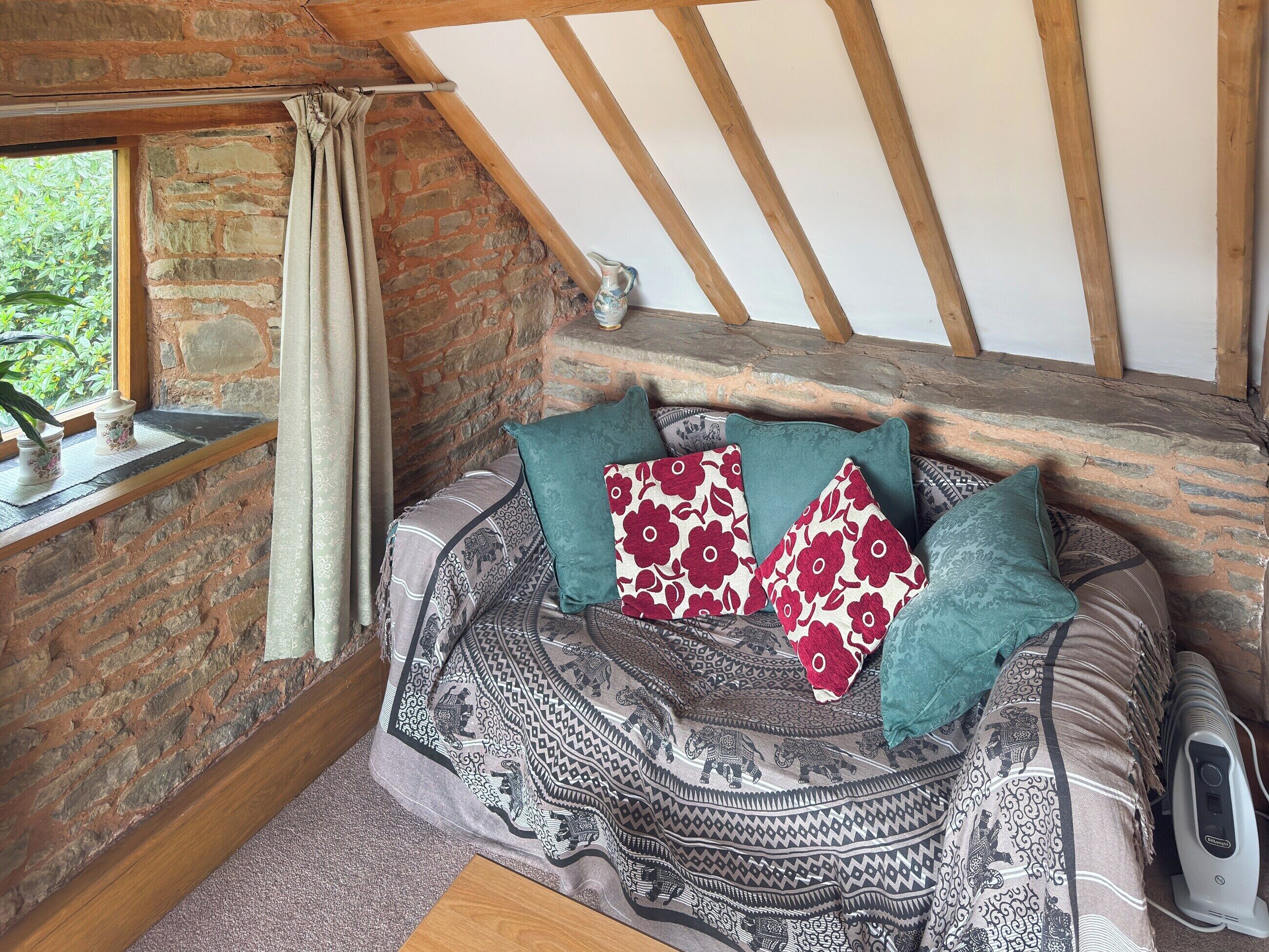 A cozy attic bedroom with a rustic stone wall, a wooden ceiling, and a patterned sofa with decorative pillows.