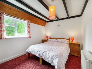 Une chambre à coucher comprenant un lit, deux lampes de chevet, une fenêtre avec des rideaux, un luminaire au plafond et un radiateur.