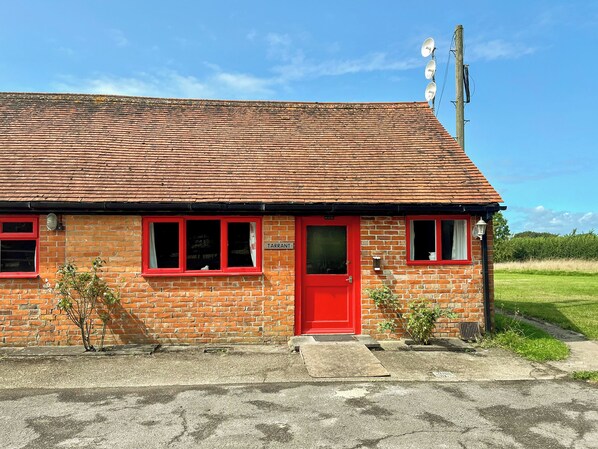 Un bâtiment en briques rouges, avec un toit recouvert de tuiles, une porte rouge et un petit porche.
