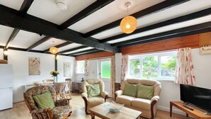 A spacious living room with wooden flooring, a sofa set, a coffee table, and a television on a wooden stand. - Tarrant Cottage -14557 (East Orchard, near Shaftesbury)
