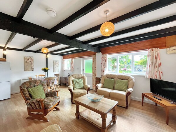 A spacious living room with wooden flooring, a sofa set, a coffee table, and a television on a wooden stand.