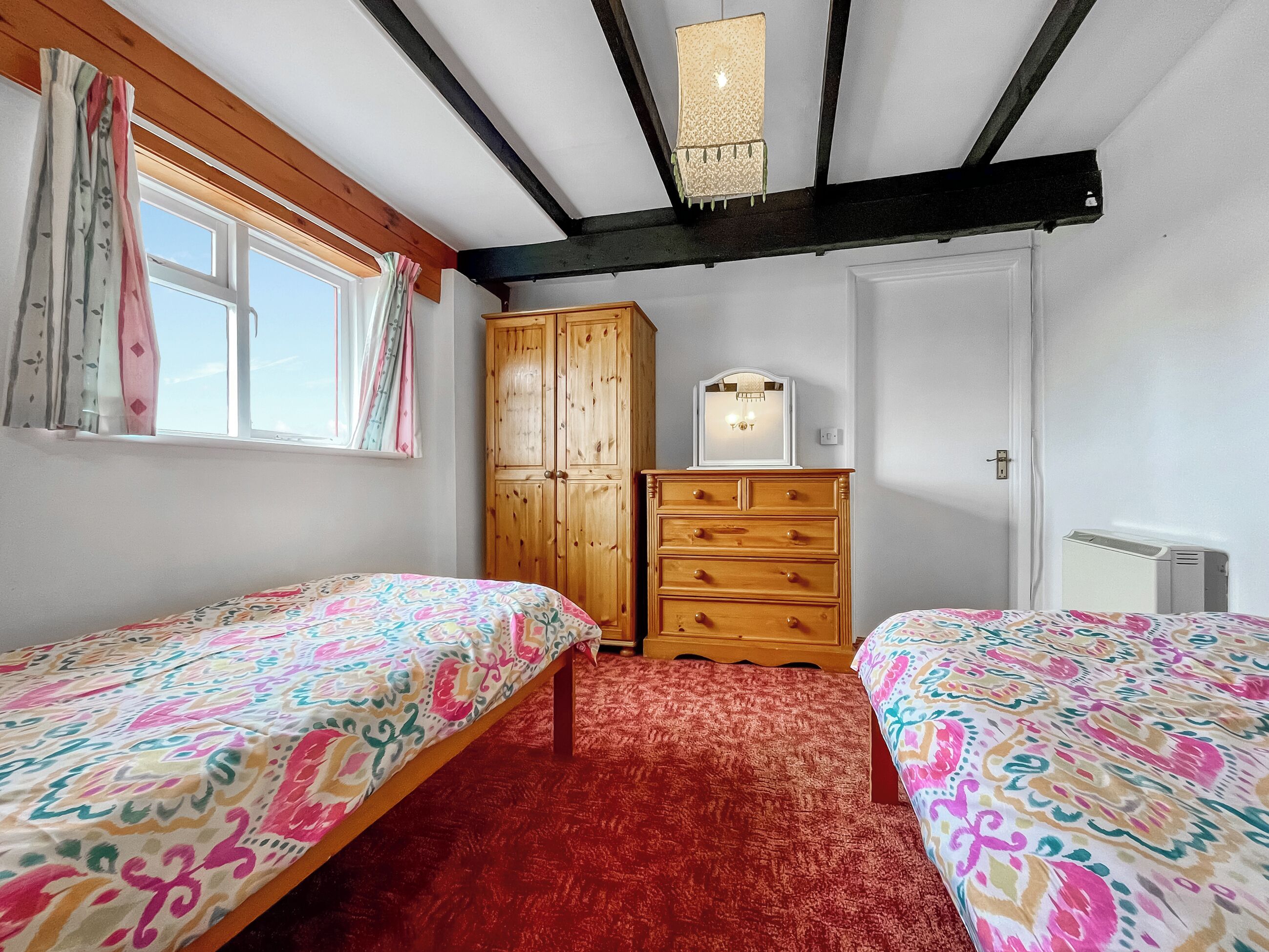 Un dormitorio con dos camas, un armario de madera, un radiador y una ventana con cortinas.