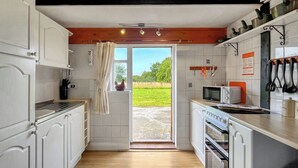 A kitchen with white cabinets, a microwave, a toaster, and a stove. There is a window with a view of greenery outside. - Tarrant Cottage -14557 (East Orchard, near Shaftesbury)