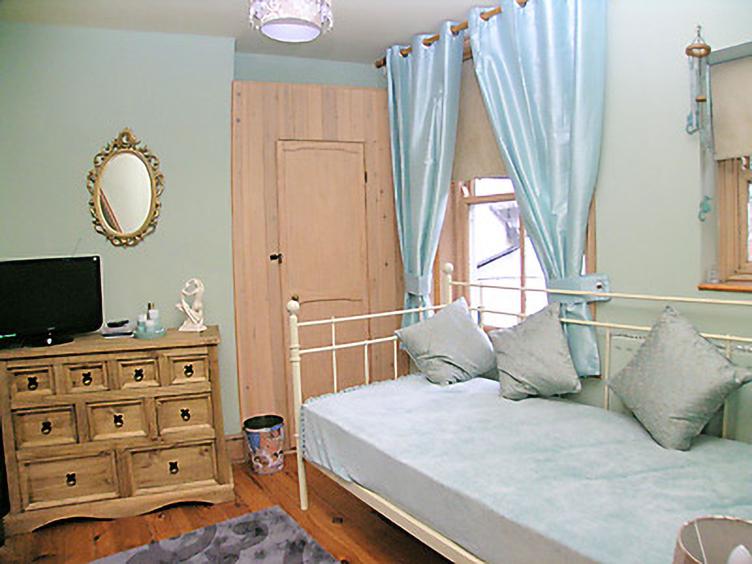 A bedroom with a bed, dresser, mirror, and a television.