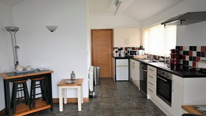 A compact kitchen with a central island, a refrigerator, a microwave, and a stove. - Orchard Farm Cottage (Barnby, near Beccles)