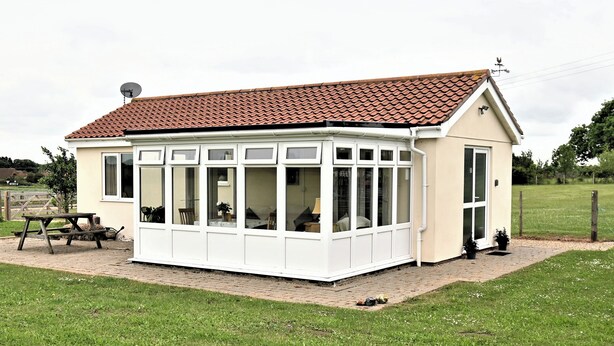 A conservatory with a tiled roof, large windows, and a small garden area with a picnic table. - Orchard Farm Cottage (Barnby, near Beccles)