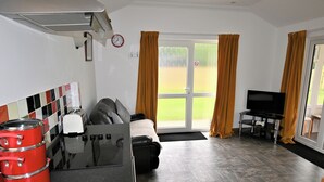 A compact hotel room with a kitchenette, a sofa bed, a television, and a sliding glass door to the outside. - Orchard Farm Cottage (Barnby, near Beccles)