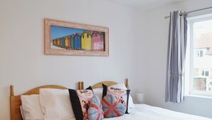 Una camera d'albergo con un letto, cuscini, un quadro appeso e una finestra con tende.