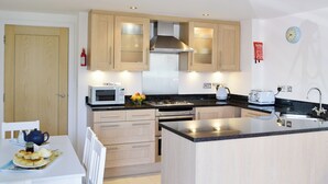 A modern kitchen with wooden cabinets, a microwave, a stove, and a sink. - 2 bedroom accommodation in West Bay, near Bridport (West Bay, near Bridport)