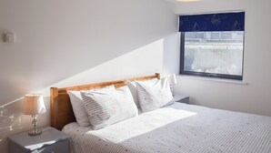 A bedroom with a bed, a nightstand, a lamp, a window with a view, and a hanging light fixture. - 2 bedroom accommodation in West Bay, near Bridport (West Bay, near Bridport)