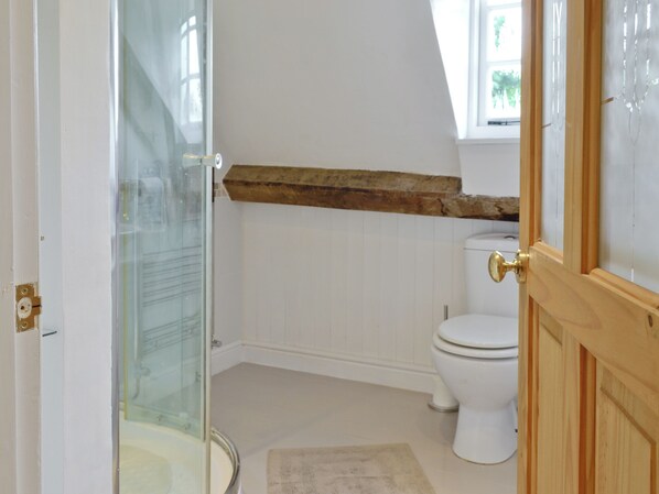 Ein Badezimmer mit Duschkabine aus Glas, einer weißen Toilette und einem Holzbalken darüber.