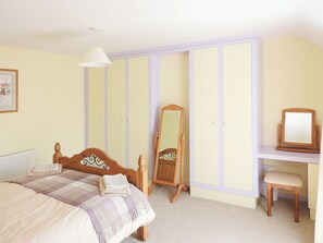 Un dormitorio con una cama, un aparador de madera, una silla, un espejo y una lámpara colgante.