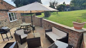 Un patio al aire libre con mobiliario de mimbre, una parrilla y un paraguas grande.