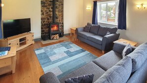 Una sala de estar acogedora con chimenea de piedra, un sofá gris, una mesa de centro de madera y un televisor de pantalla plana sobre un mueble de madera.