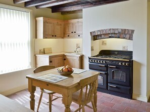 Una cocina con armarios de madera, una estufa y una mesa de comedor con un cuenco de fruta.
