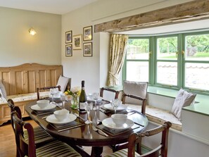 Un comedor con una mesa de madera preparada para cuatro personas, rodeada de sillas, un banco y una ventana con cortinas.