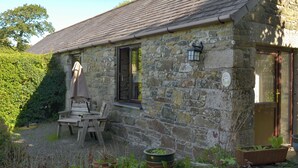 A stone cottage with a tiled roof, a wooden table and chairs outside, and a garden with potted plants. - 1 bedroom accommodation in Michaelstow, near Camelford (Michaelstow, near Camelford)