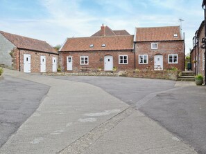 En traditionell byggnad i tegel med ett tak täckt av takpannor, flera dörrar och en stenlagd innergård.