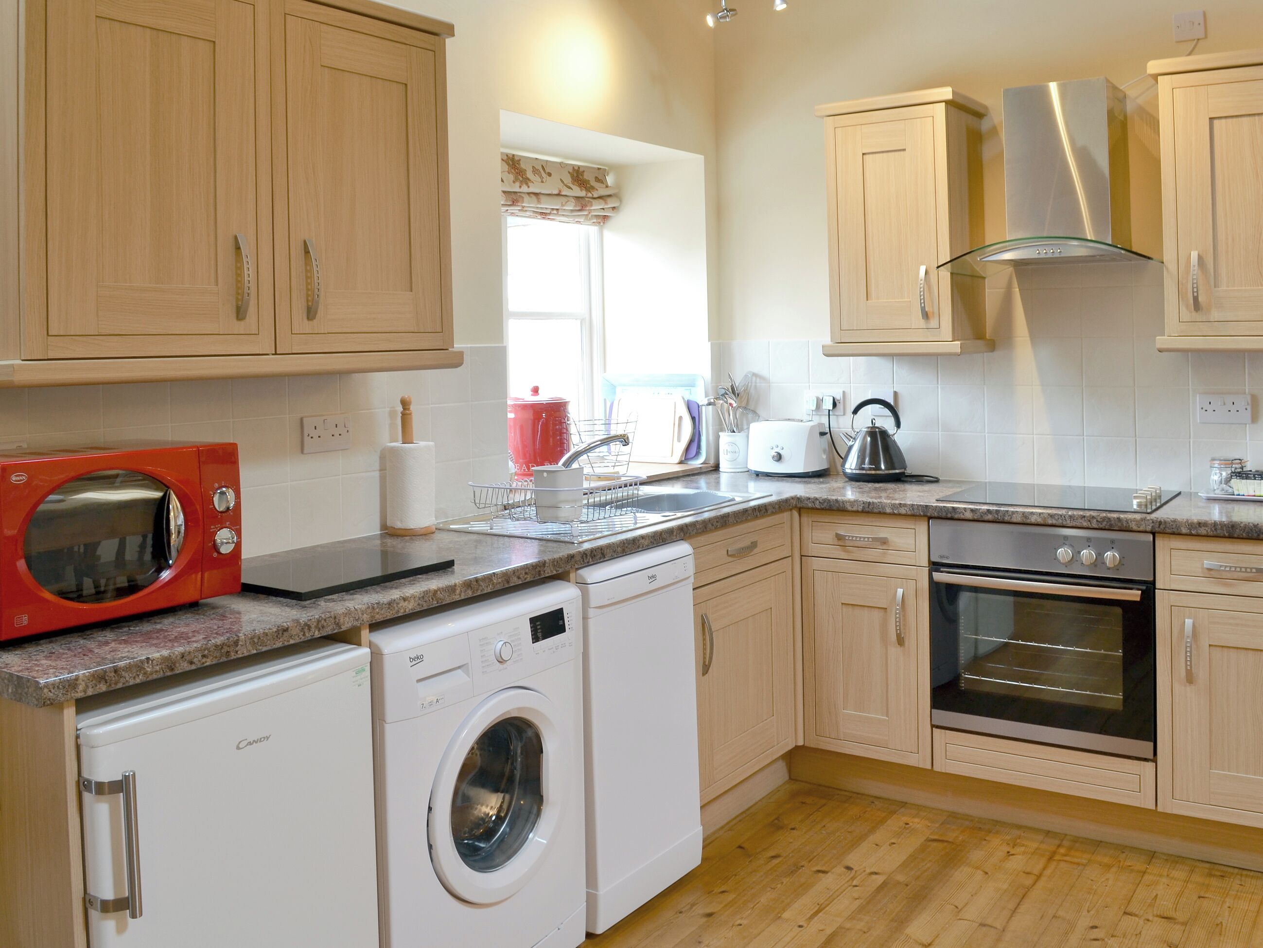 A compact kitchen with wooden cabinets, a microwave, a washing machine, a toaster, and an oven.