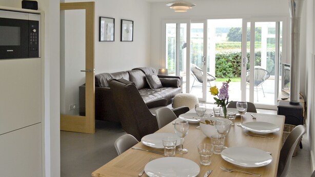 A modern kitchen with a built-in microwave, a dining area with a wooden table set for four, and a grey sofa in the background. - 3 bedroom accommodation in Brancaster Staithe, near Hunstanton (Brancaster Staithe, near Hunstanton)