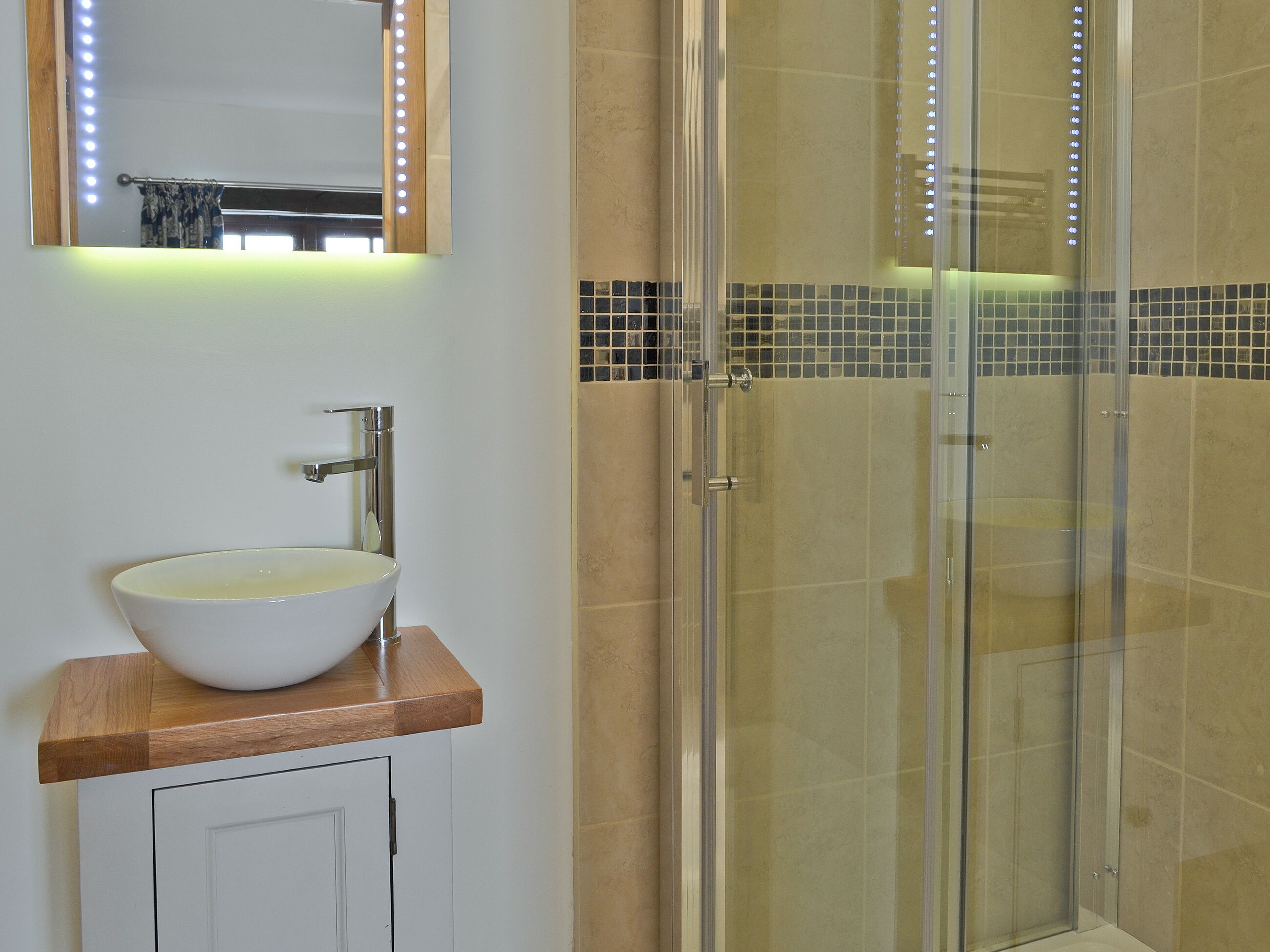 A bathroom with a white sink, a mirror with lights, and a glass shower enclosure.
