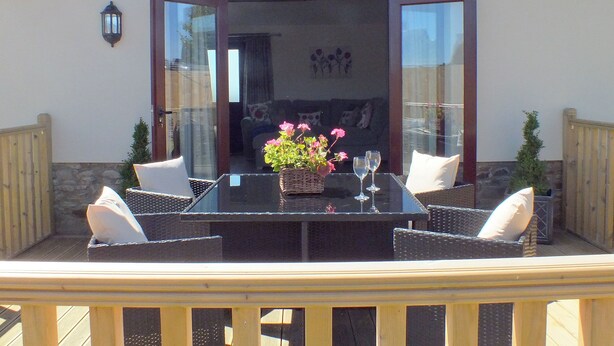 Un patio exterior con una mesa, sillas, un jarrón de flores y vistas al interior a través de puertas de cristal.